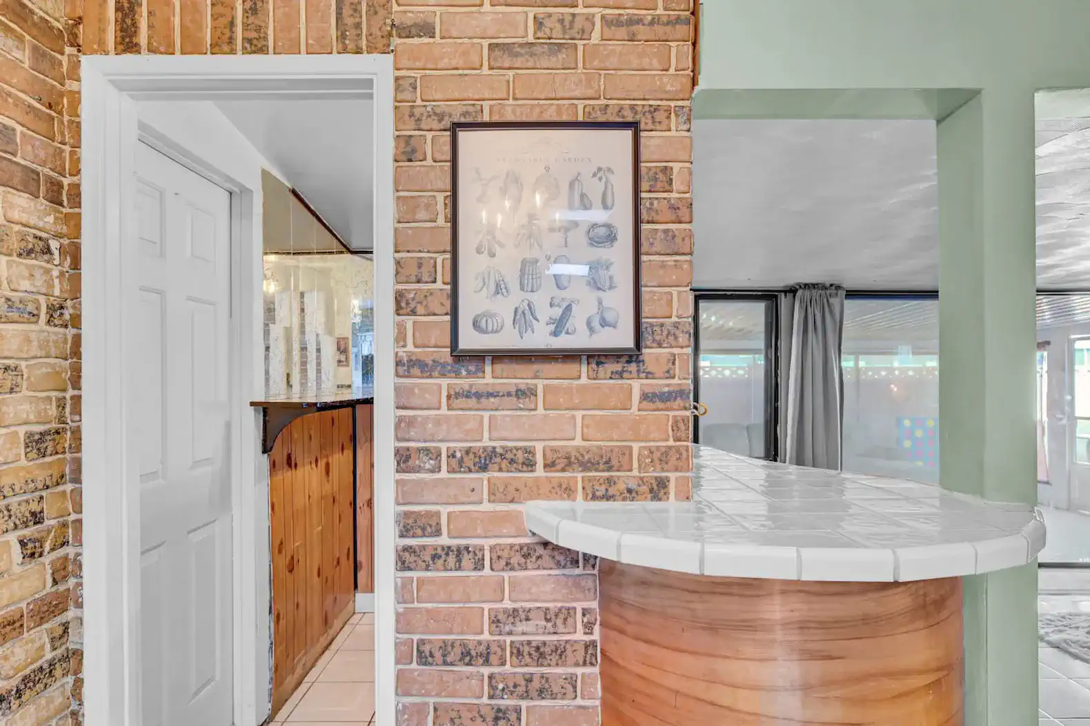 Brick wall with framed artwork and a bar counter leading to another room