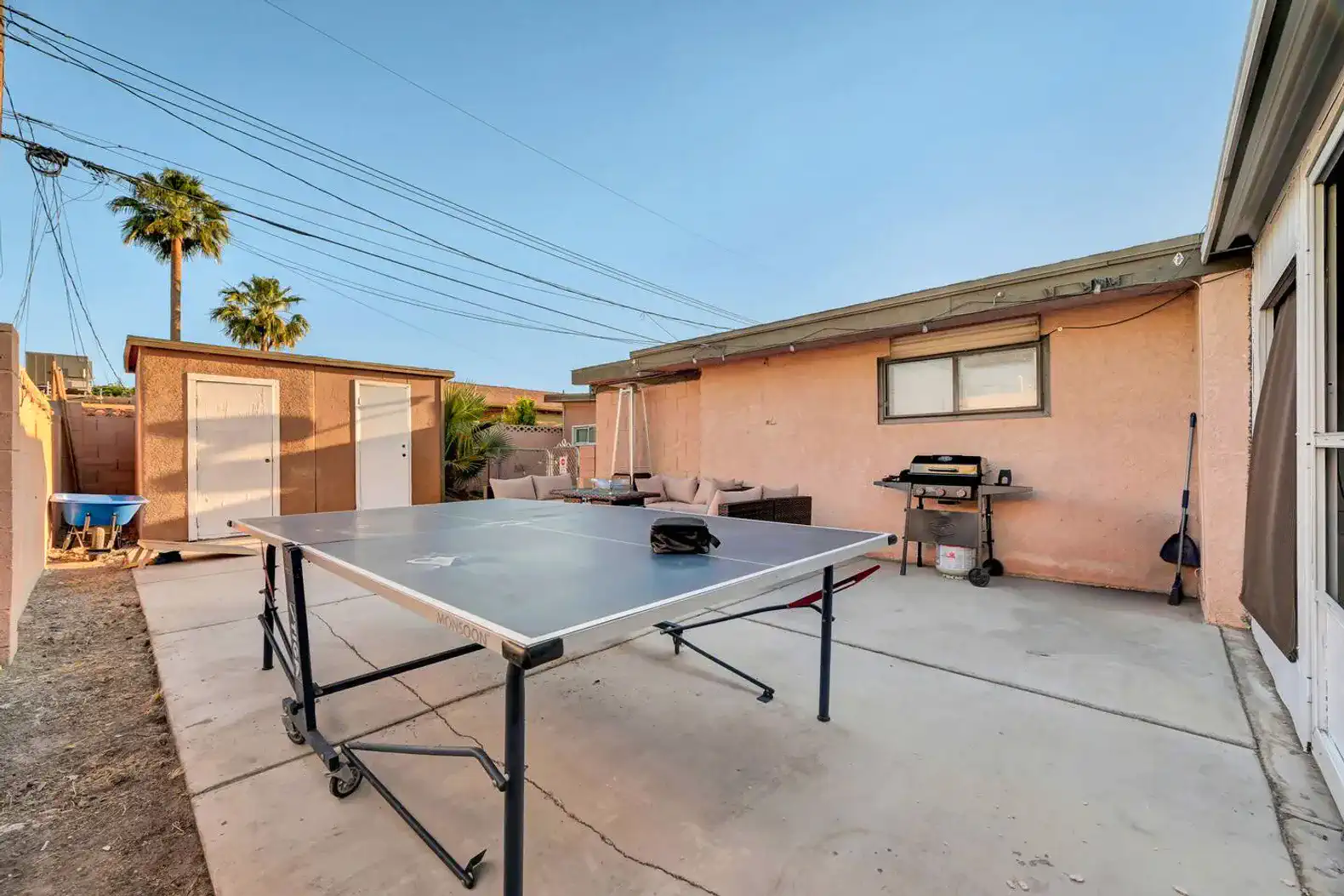 Outdoor area featuring a ping pong table and seating with palm trees in the background