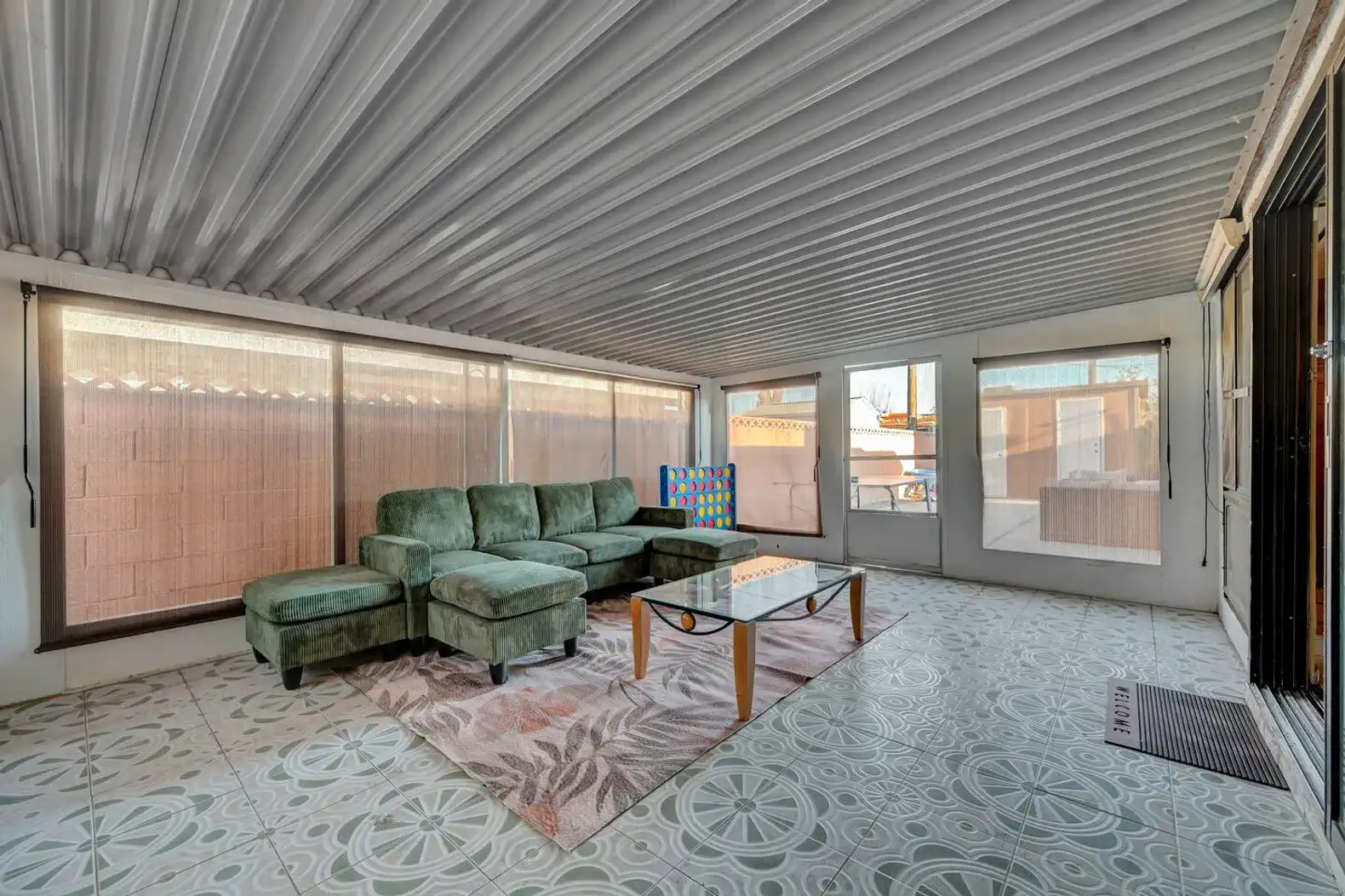 Bright and spacious sunroom with green sectional sofa and large windows