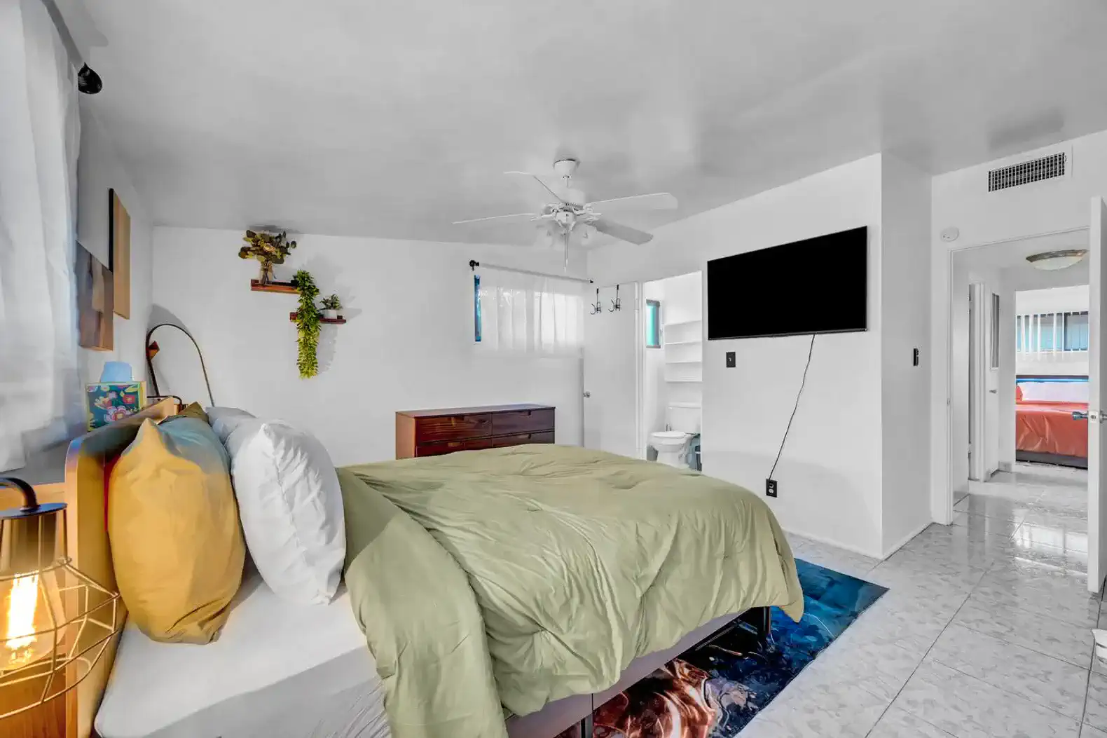 Cozy master bedroom with a green comforter, ceiling fan, and wall-mounted TV