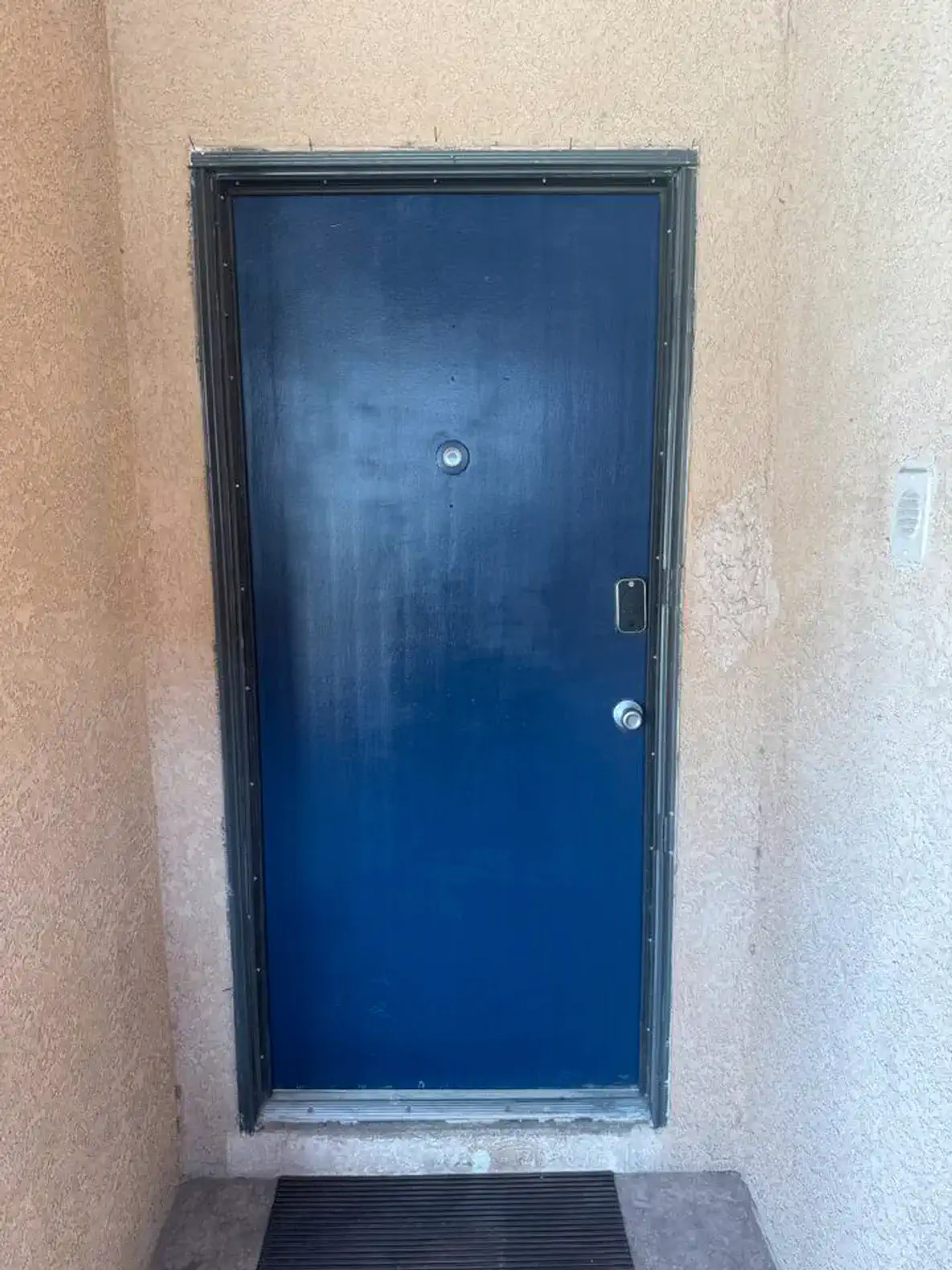 Solid blue front door with a peephole and textured wall surrounding it