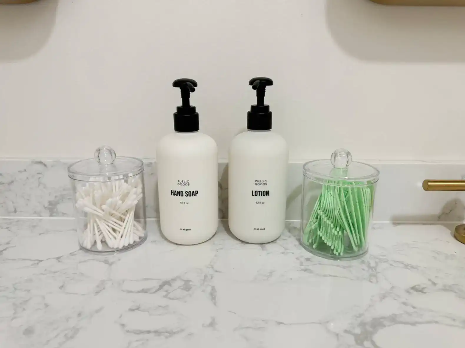 Bathroom countertop with hand soap and lotion dispensers alongside cotton swabs and pads