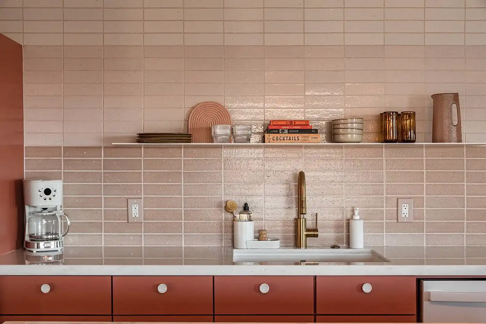 Modern kitchen with pink tile backsplash, brass faucet, and stylish decor on shelves