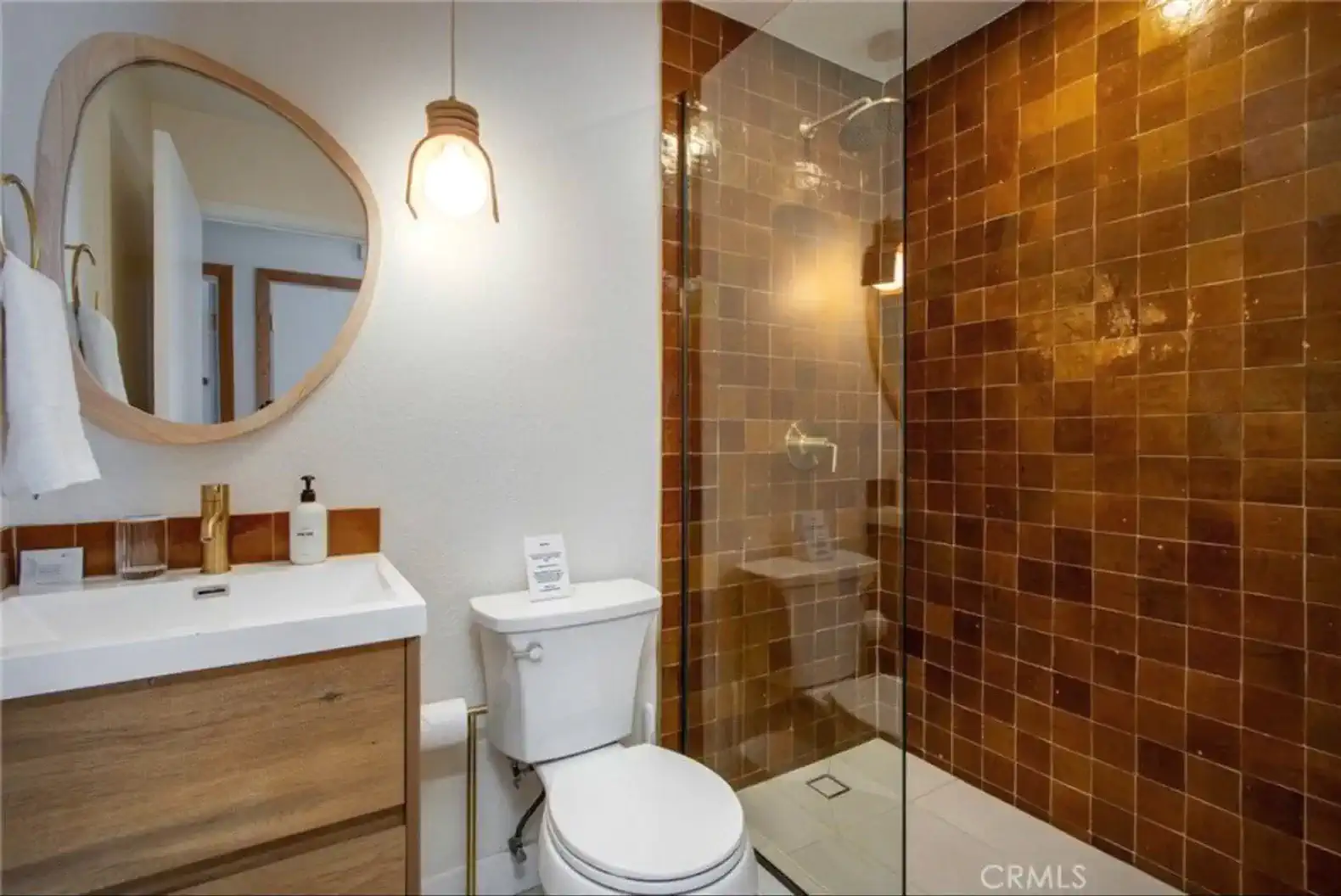 Modern bathroom featuring a walk-in shower with brown tiles and a stylish round mirror