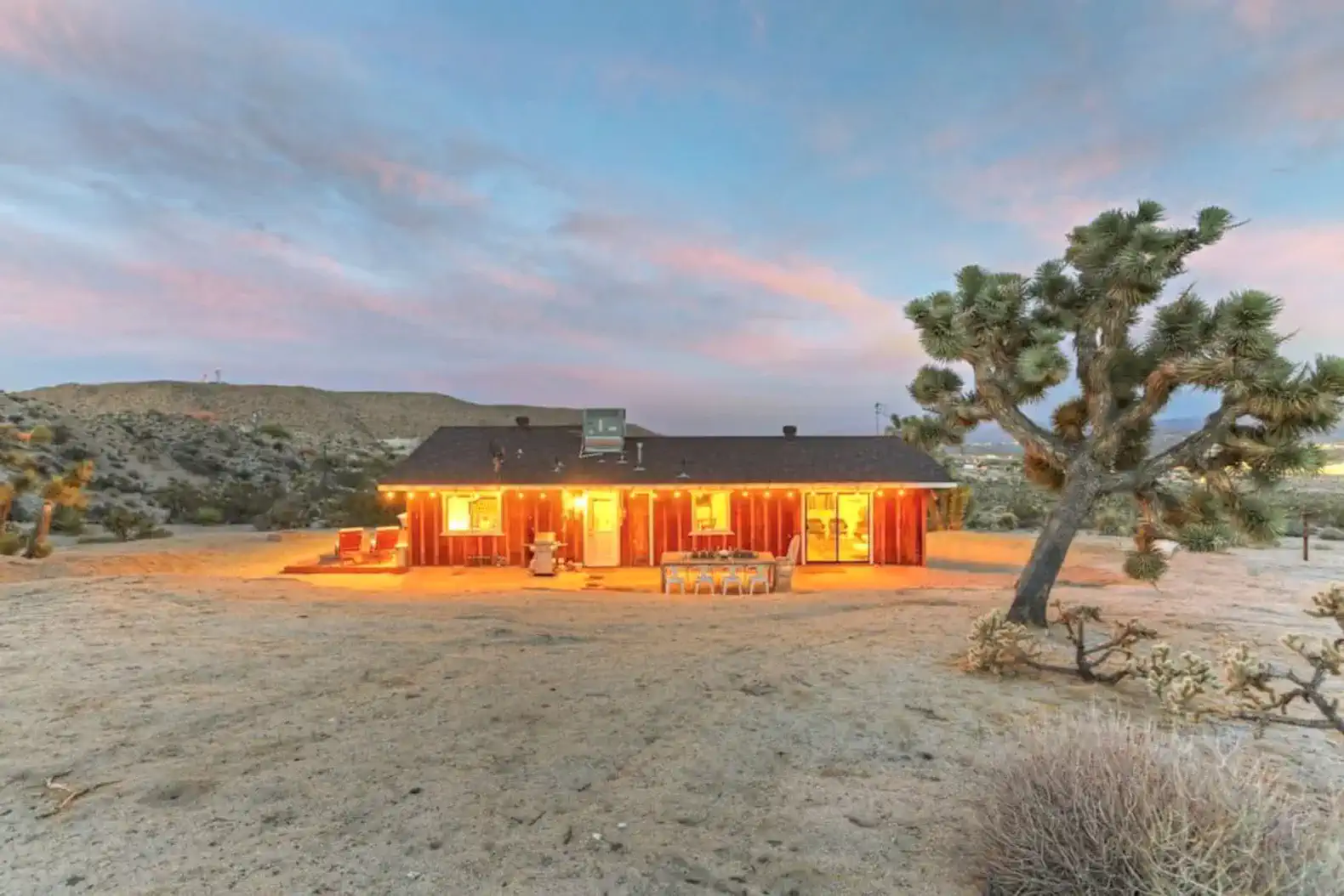 Cozy cabin exterior with warm lights and desert landscape at sunset