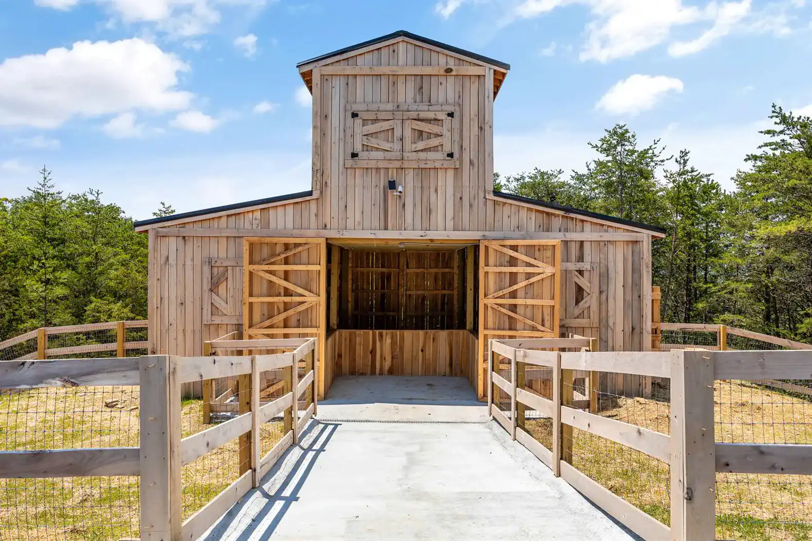 Rustic wooden barn with open doors and a fenced pathway