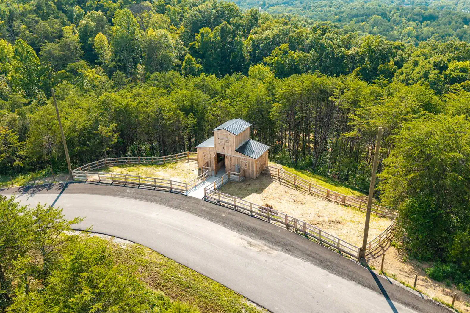 Aerial view of a rustic cabin surrounded by trees and a fenced area