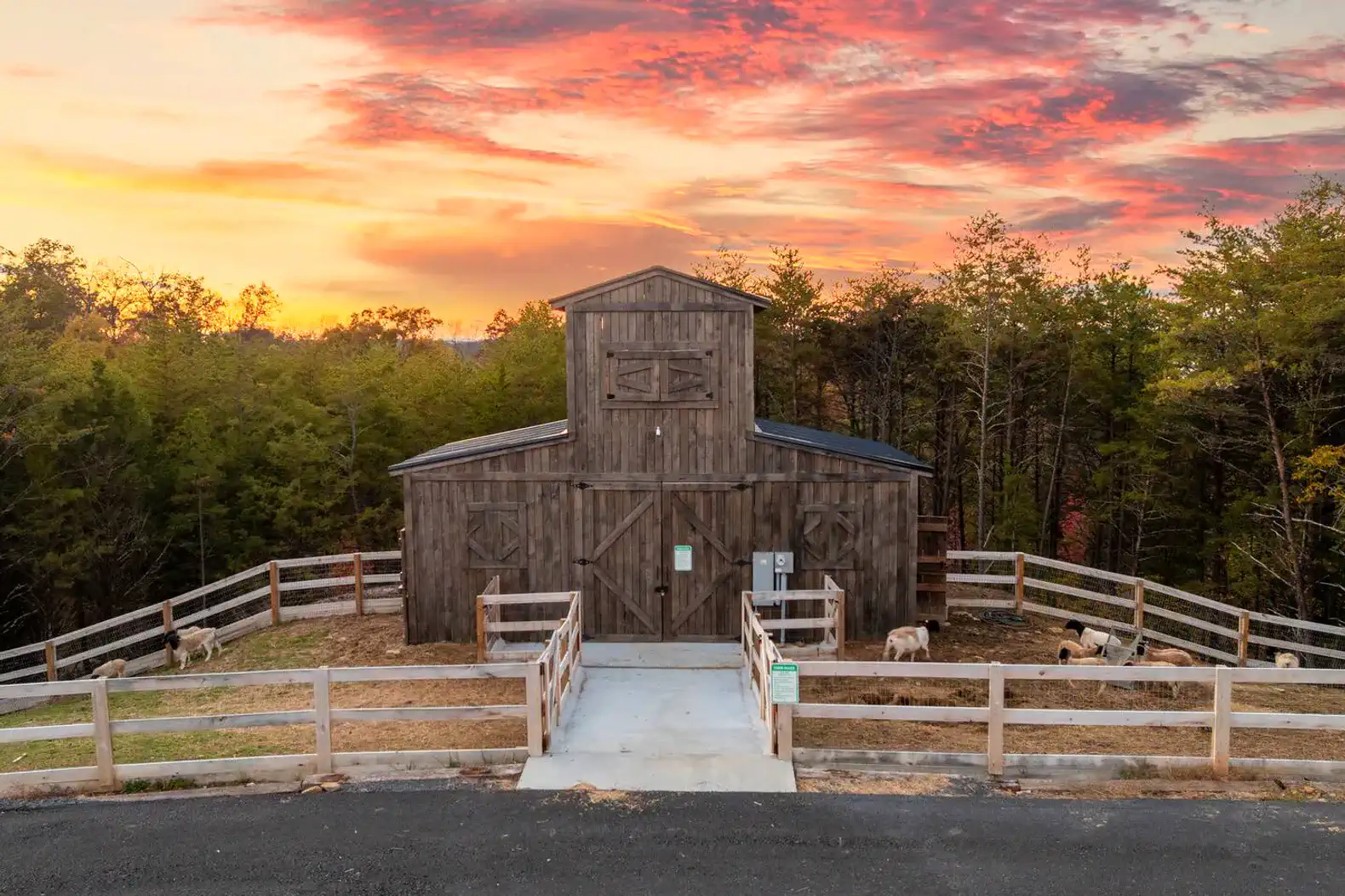 Rustic barn surrounded by wooden fencing and trees at sunset