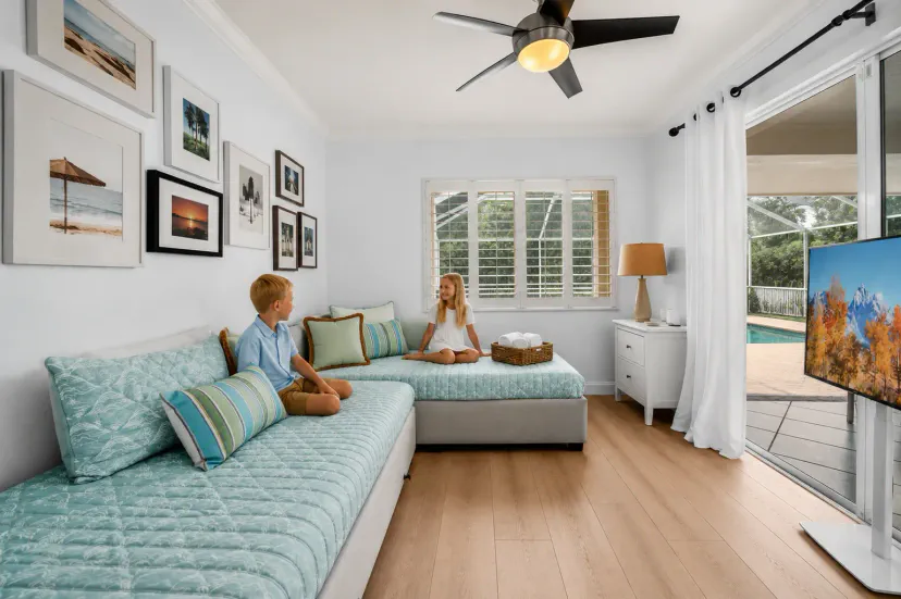 A bright, versatile den designed for relaxation and fun, with two cozy daybeds and an extra trundle, a TV for movie nights, and direct access to the pool just steps away.