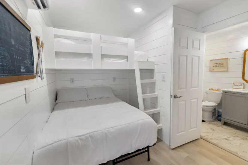 Bright coastal bunk room with queen bed, twin bunks, and ensuite bath