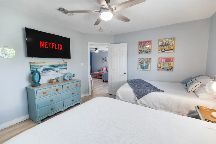 Bright coastal bedroom with two beds, streaming TV, and cheerful beach decor