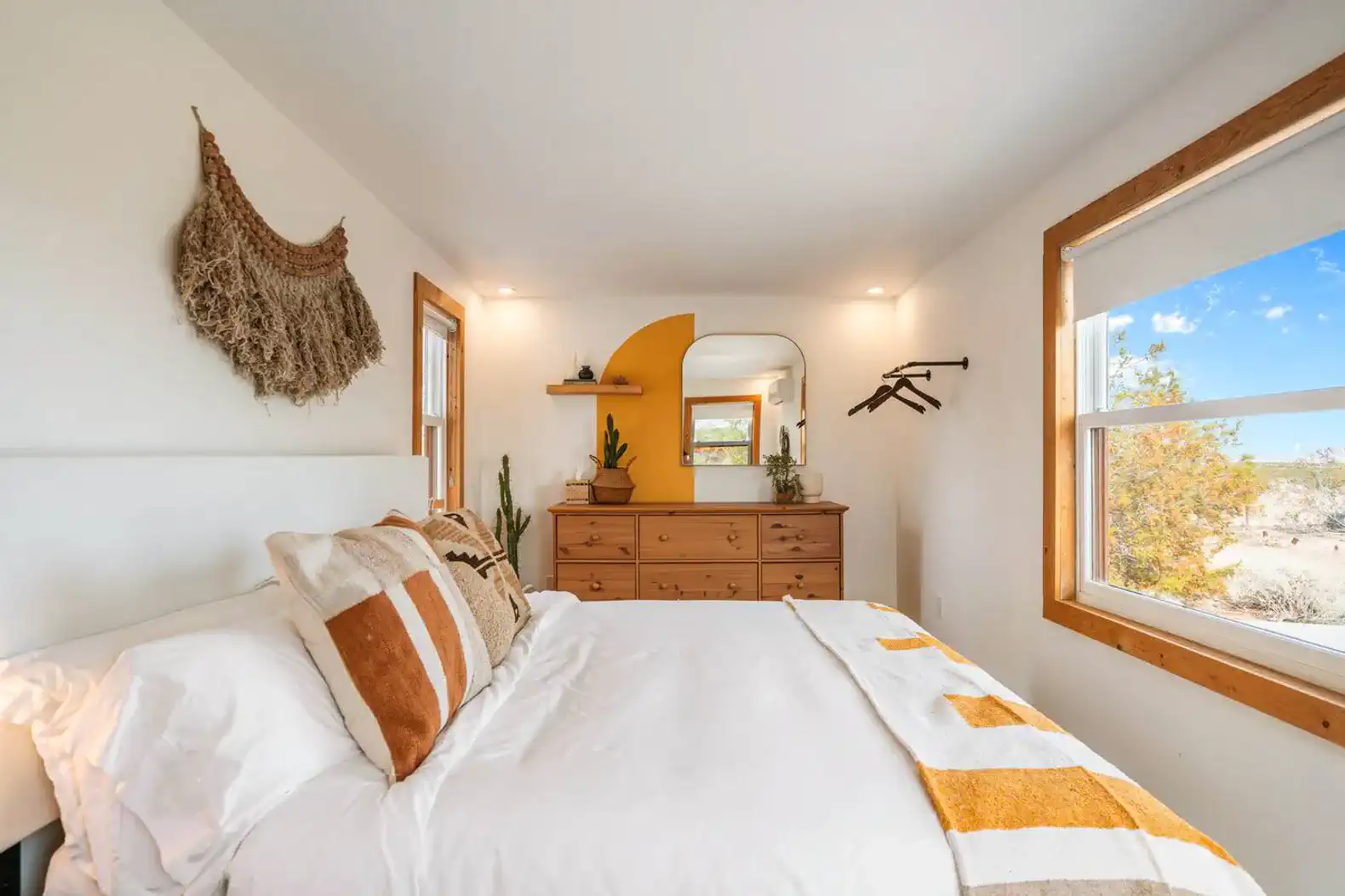 Cozy master bedroom with a white bed, wooden dresser, and desert views