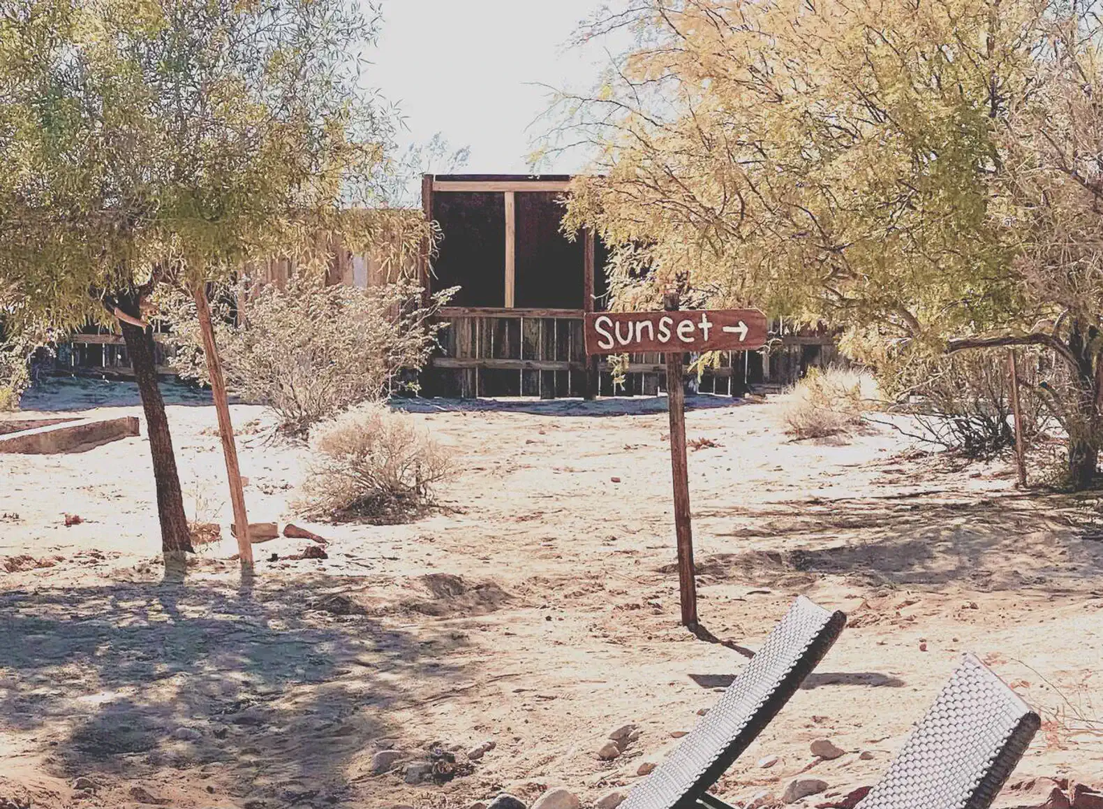 Signpost indicating direction to sunset with desert landscape and sparse vegetation