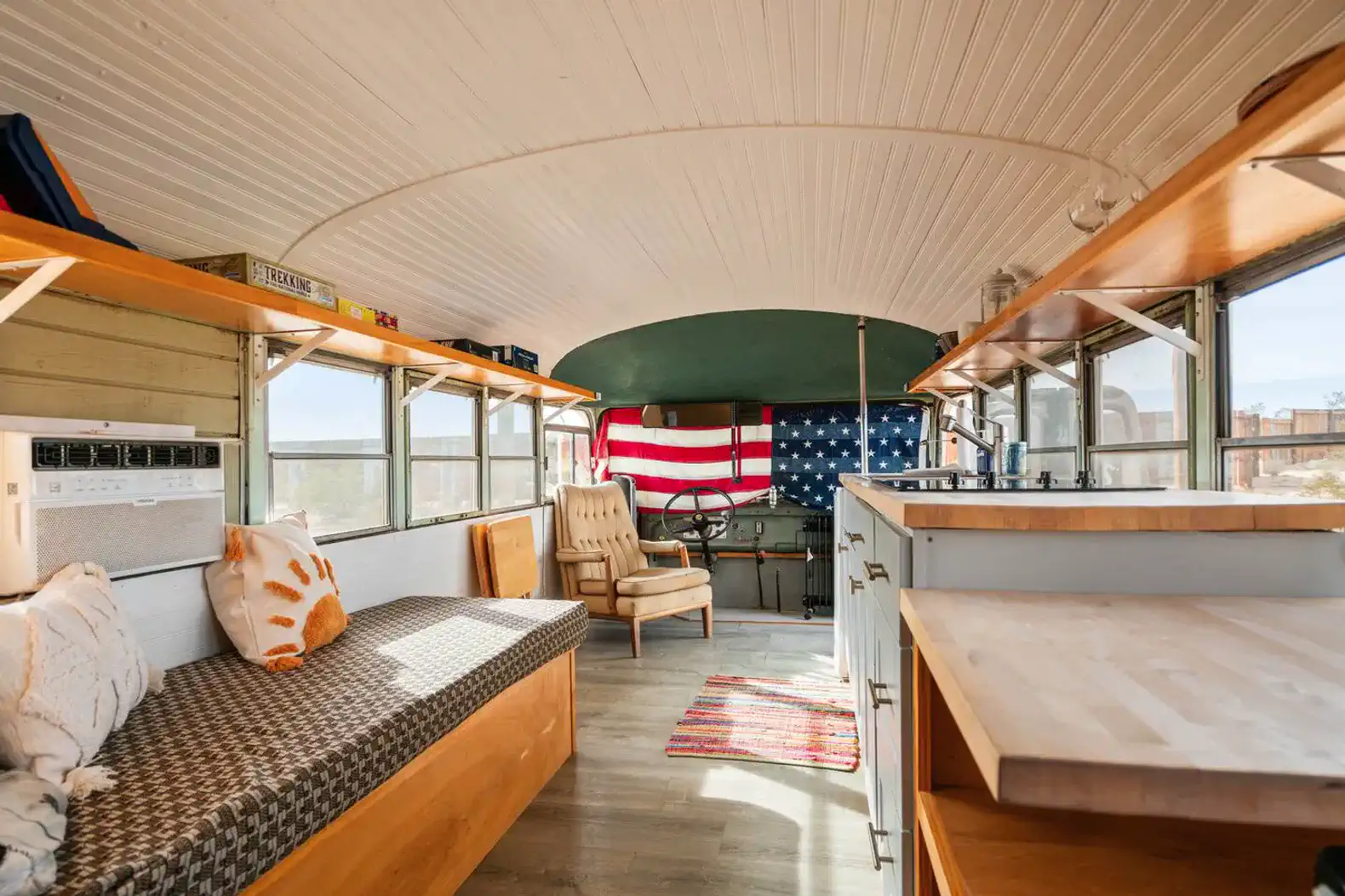 Cozy interior of a converted bus with seating, kitchenette, and decorative flags