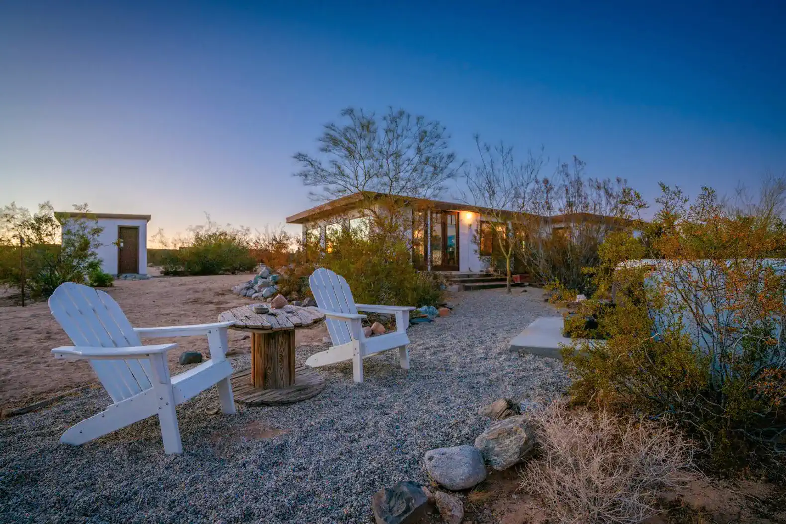 Cozy outdoor seating area with white chairs and a fire pit surrounded by desert landscape