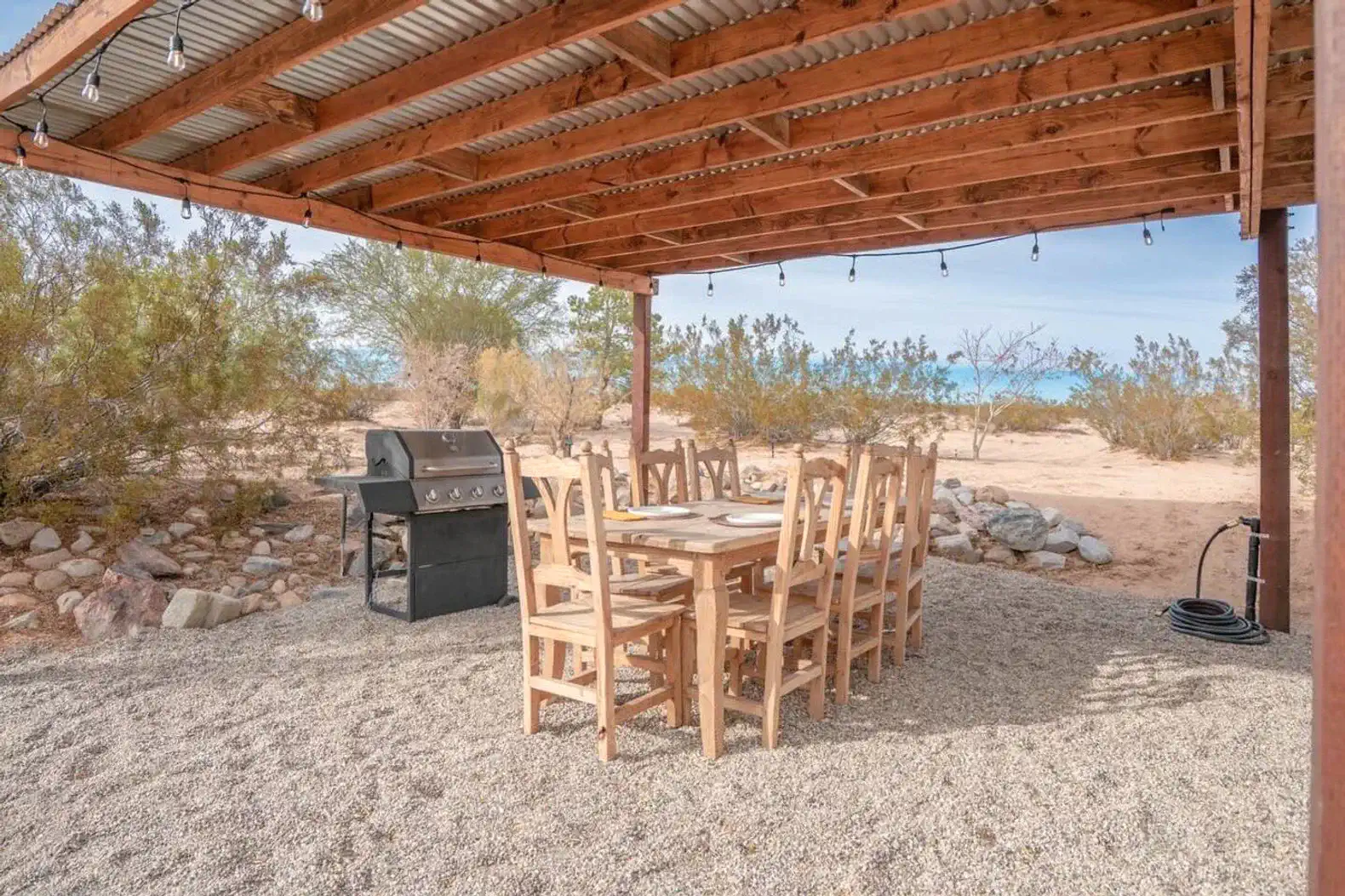 Outdoor dining area with a large table and grill under a wooden pergola