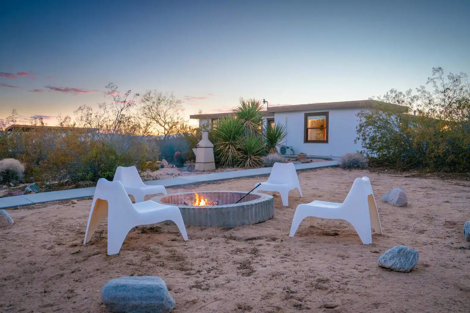 Cozy outdoor fire pit area with white chairs surrounded by desert landscape