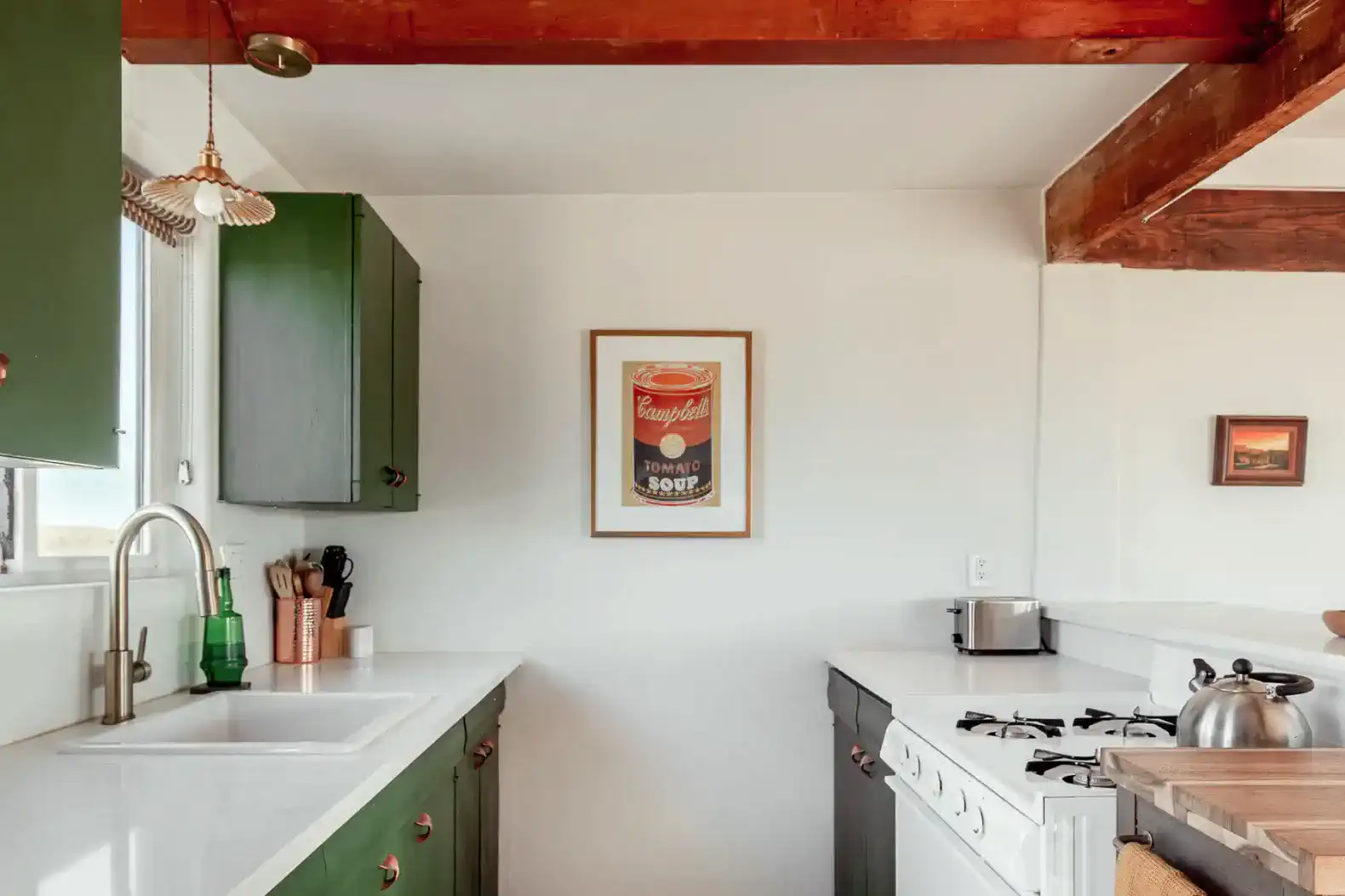 Modern kitchen with green cabinets, white countertops, and vintage soup can artwork