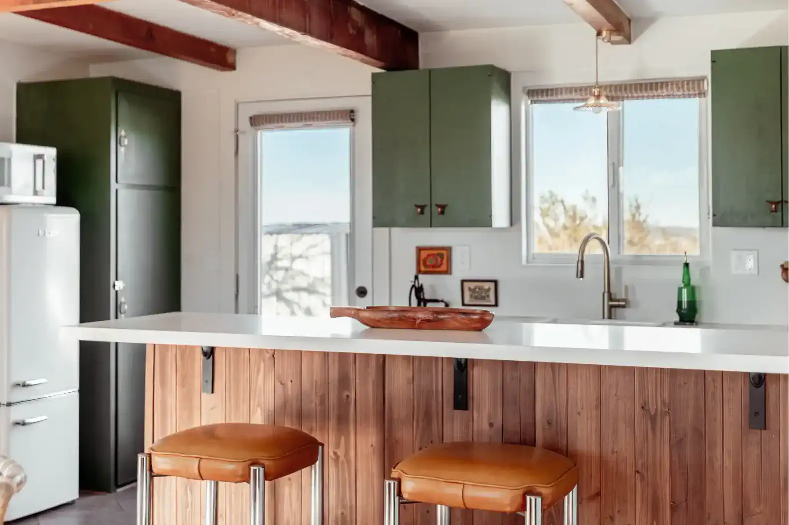 Modern kitchen with green cabinets, white countertops, and bar stools