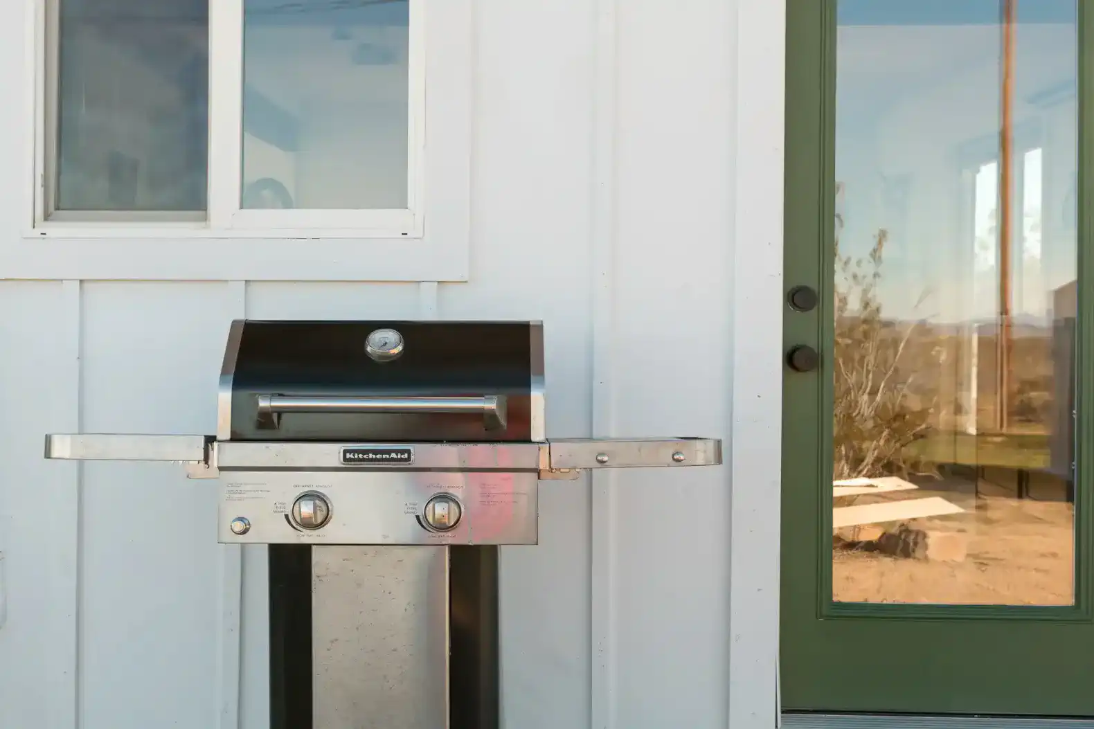 Outdoor grill next to a green door with a reflection of the landscape