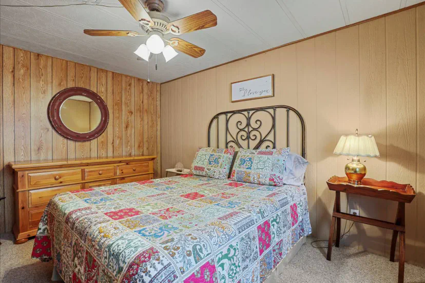 Quarto aconchegante com um edredom colorido, cômoda de madeira e ventilador de teto