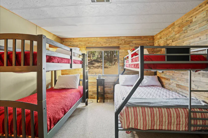 Quarto de beliche aconchegante com dois conjuntos de beliches e uma cama queen, com detalhes rústicos em madeira
