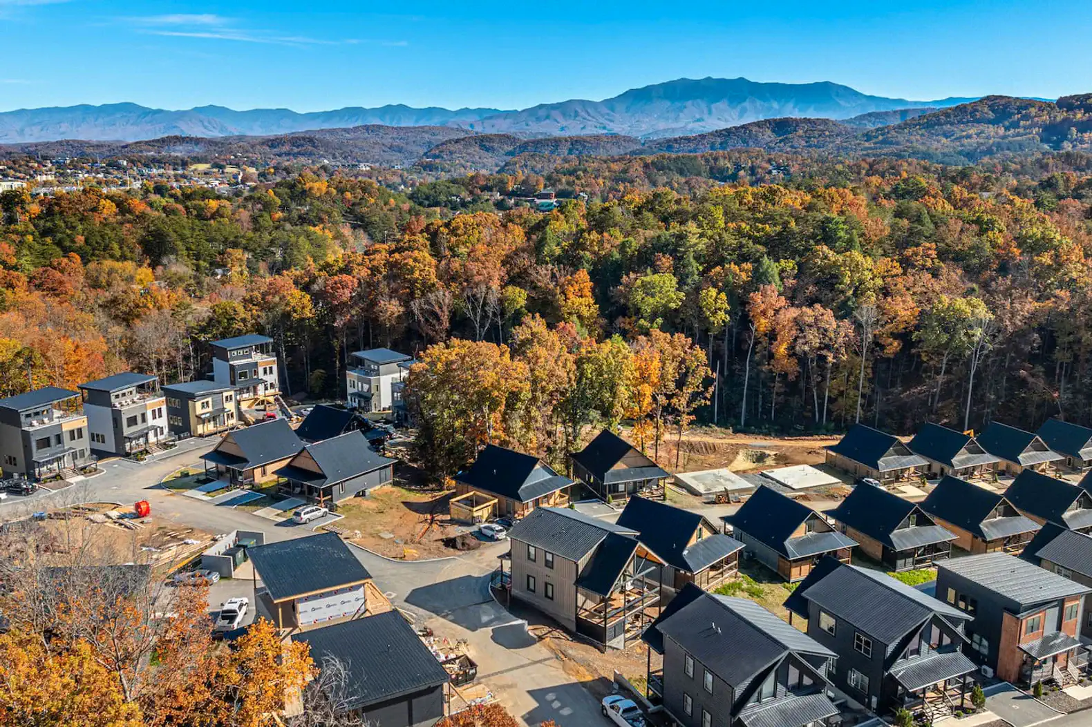 Aerial view of a neighborhood surrounded by colorful autumn trees and mountains in the background