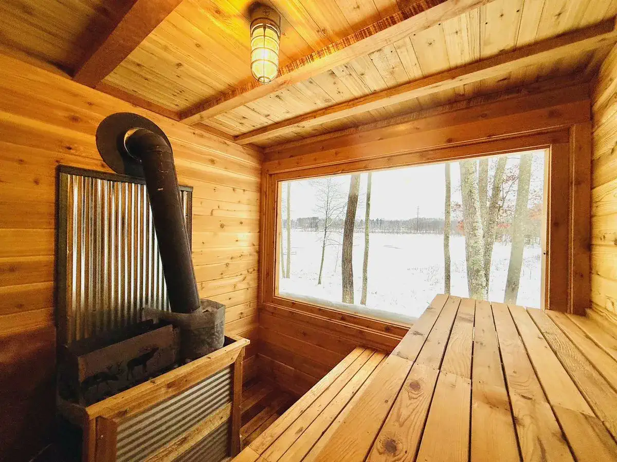 Cedar sauna interior with a wood-fired stove and a large window looking out on a snowy lake