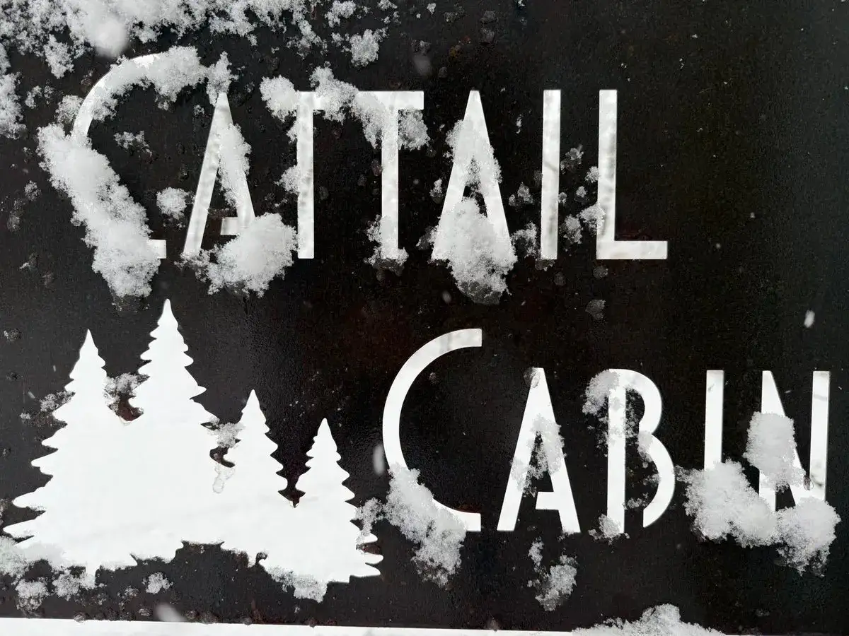 Snow-dusted Cattail Cabin sign at O'Connell Cabin Co. on Lower Holly Lake in winter