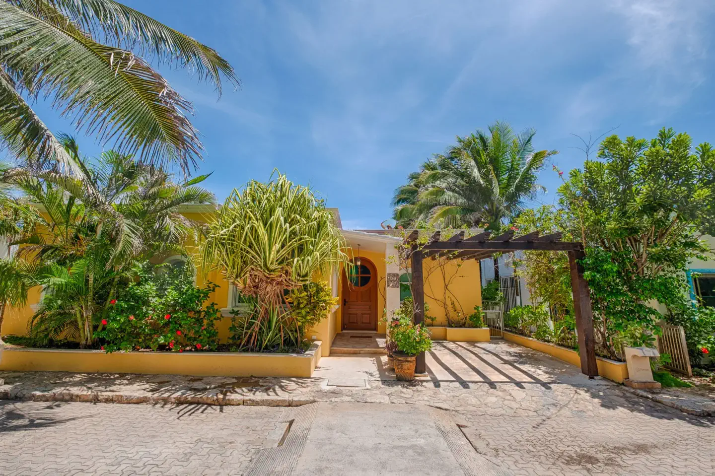 The street entrance to Casa Karma, with yellow walls, a wooden front door, and tropical plants