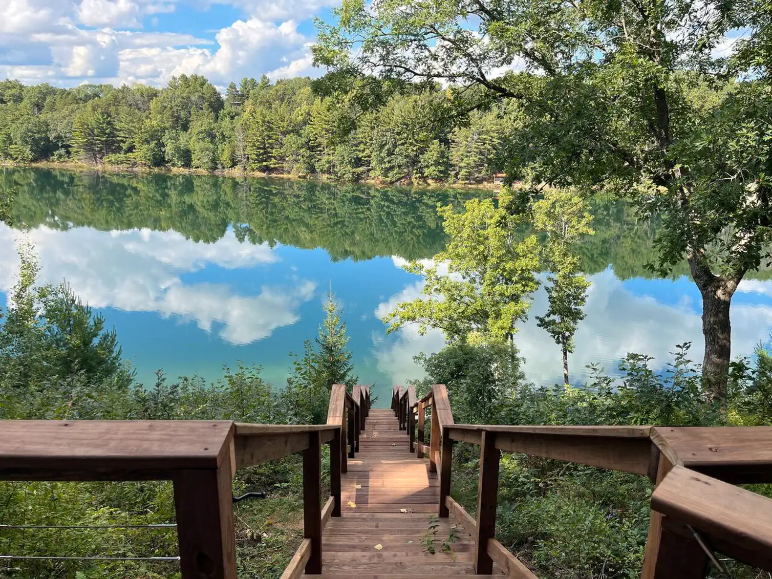 Brand-new stairs lead down to the lake—over 100 steps with safe railings and comfortable spacing. They end at a small open landing above the water, as the pier has been removed. Access the stairs by walking around the back of the house.