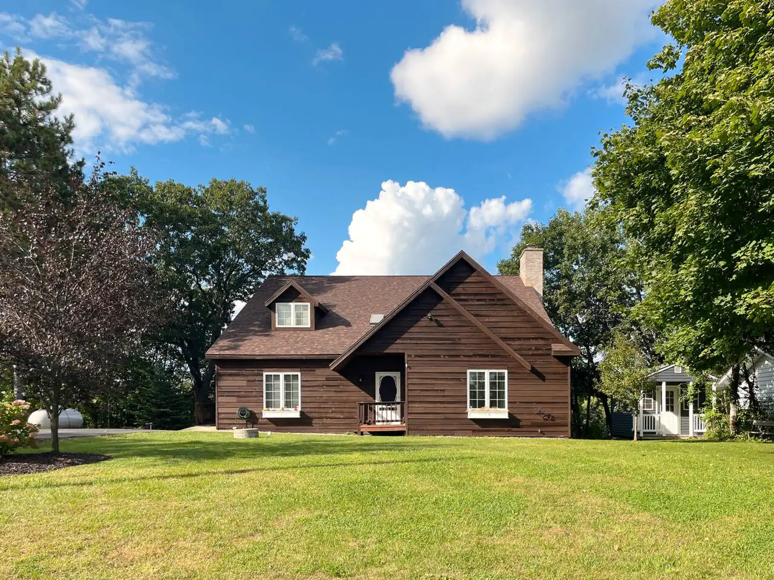 Charming brown house with a large lawn and trees under a blue sky