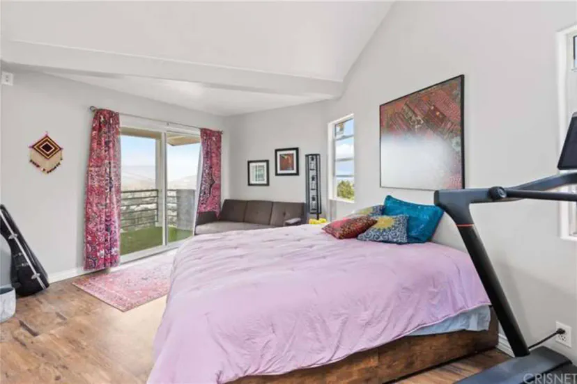 The focal point is a plush bed dressed in rich purple bedding and pillowcases, creating a striking contrast against the white walls and ceiling.