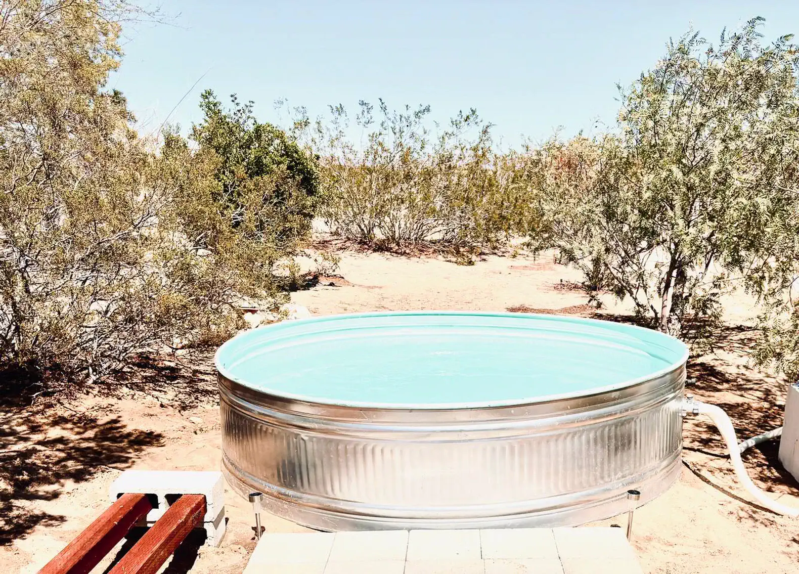 Round metal soaking tub surrounded by desert vegetation