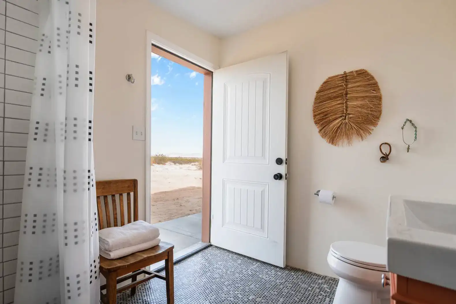 Bright bathroom with a door leading to outdoor desert views and a wooden chair