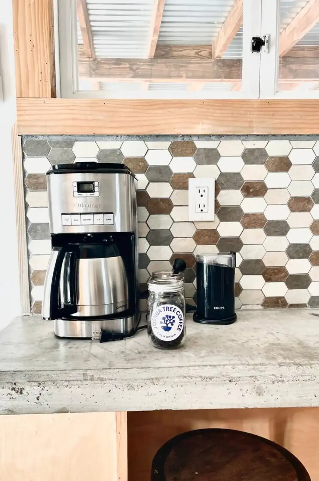 Coffee maker and grinder on a countertop with a hexagonal tile backsplash