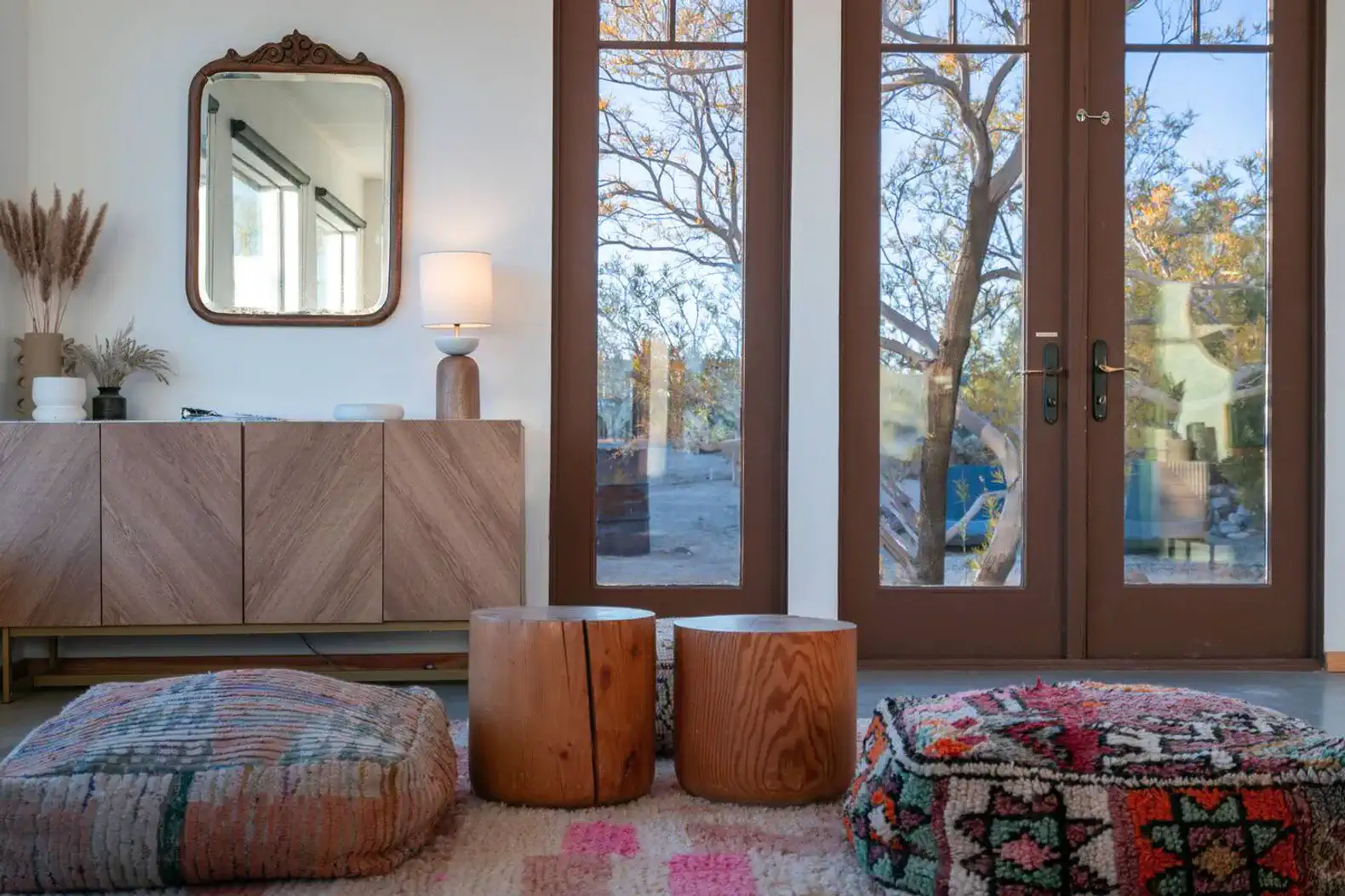 Cozy living area with wooden stools and colorful rugs near large glass doors