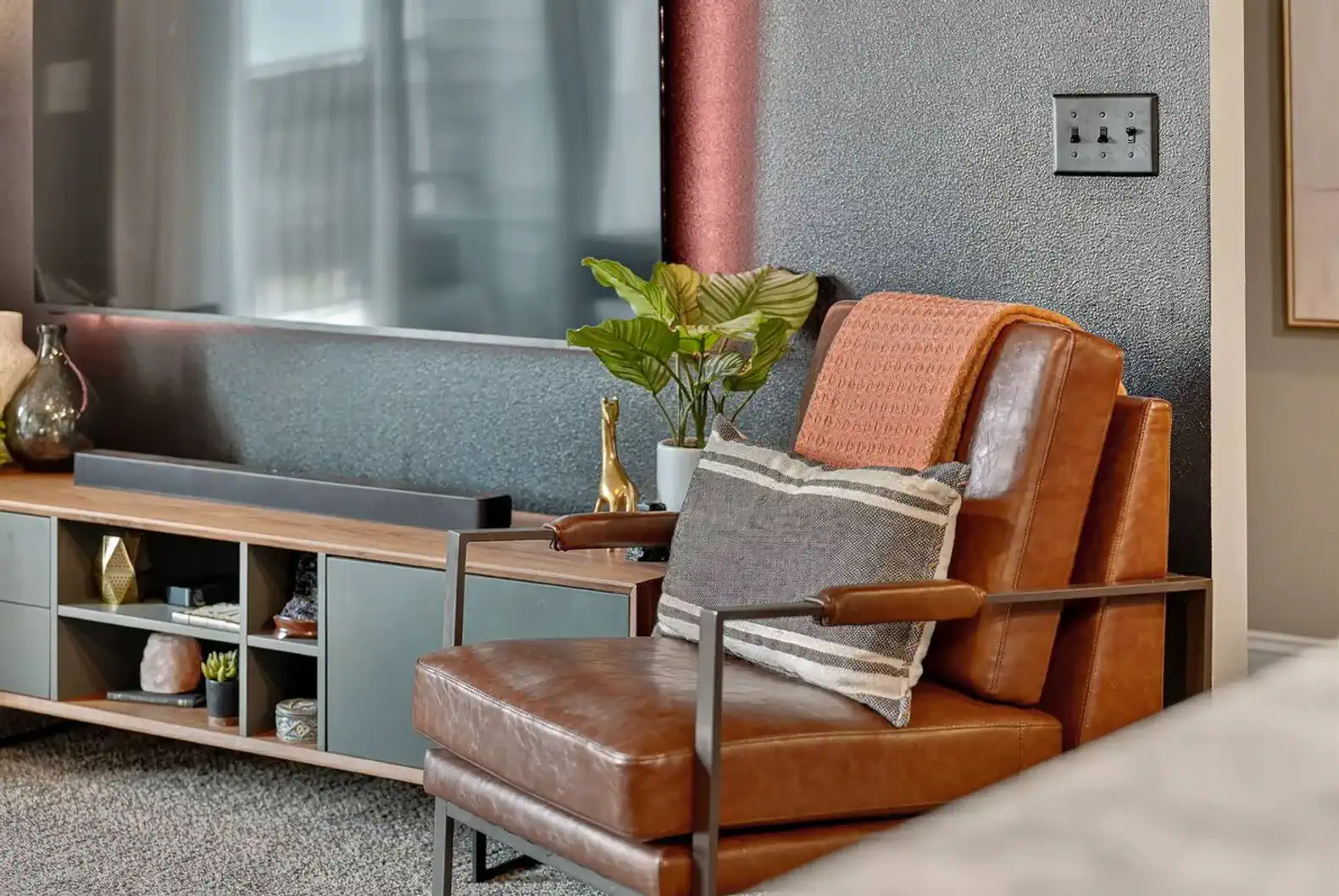 Modern media console and leather chair with décor accents. Custom touches transform this space into a chic condo-inspired retreat.