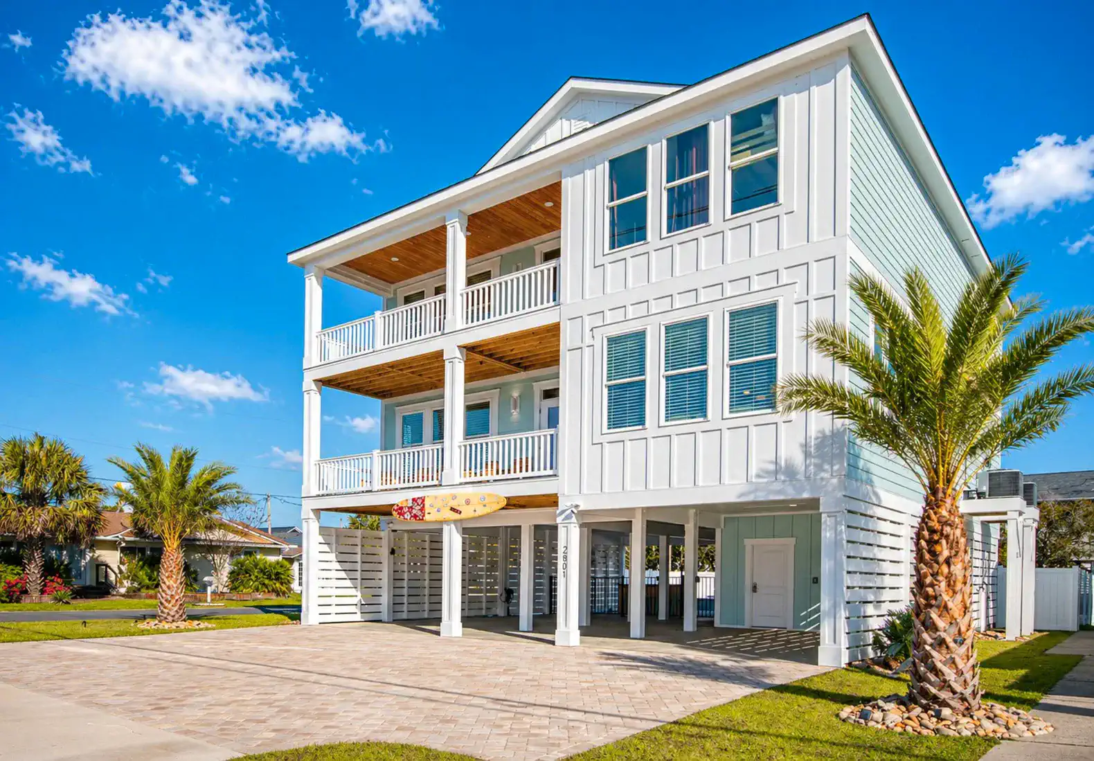 Spacious white beach house with multiple balconies and palm trees in front