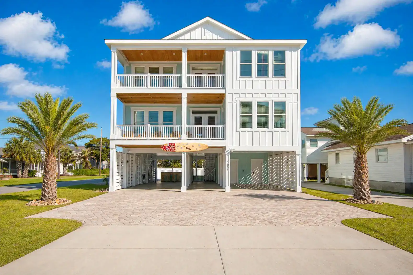 Three-story beach house with large balconies and palm trees in front
