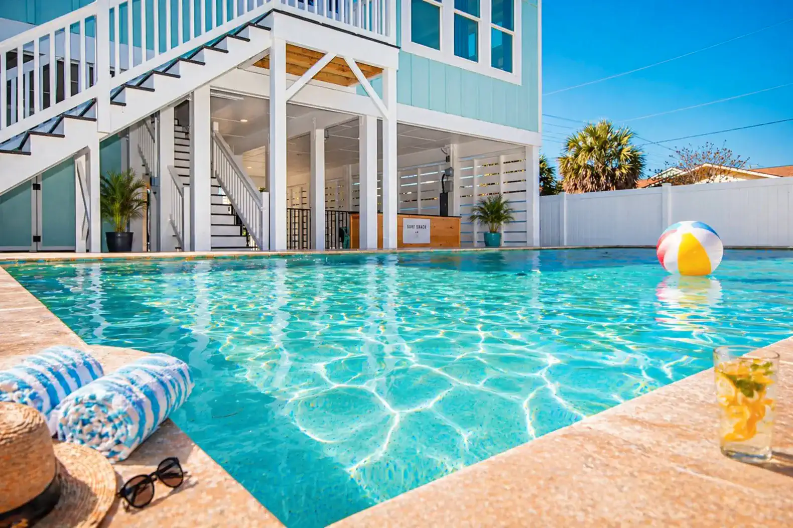 Heated pool with colorful beach ball and towels, surrounded by a modern home