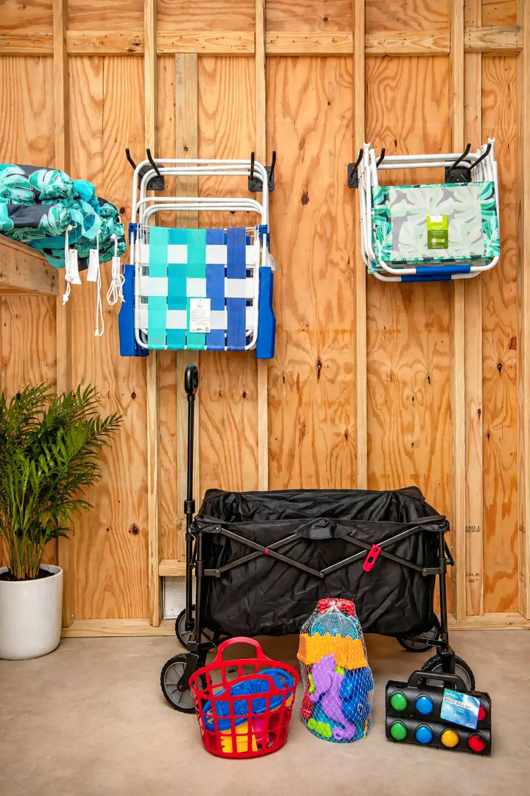 Storage area with beach chairs, toys, and a cart against a wooden wall