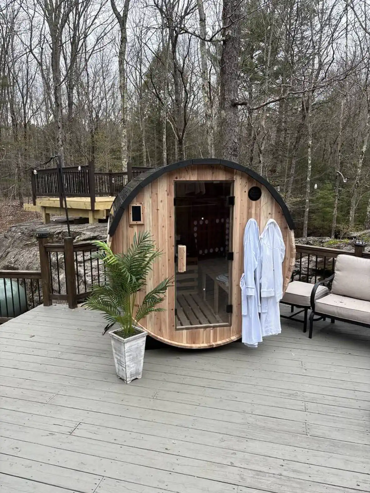 Wooden sauna on a deck surrounded by trees with robes hanging outside