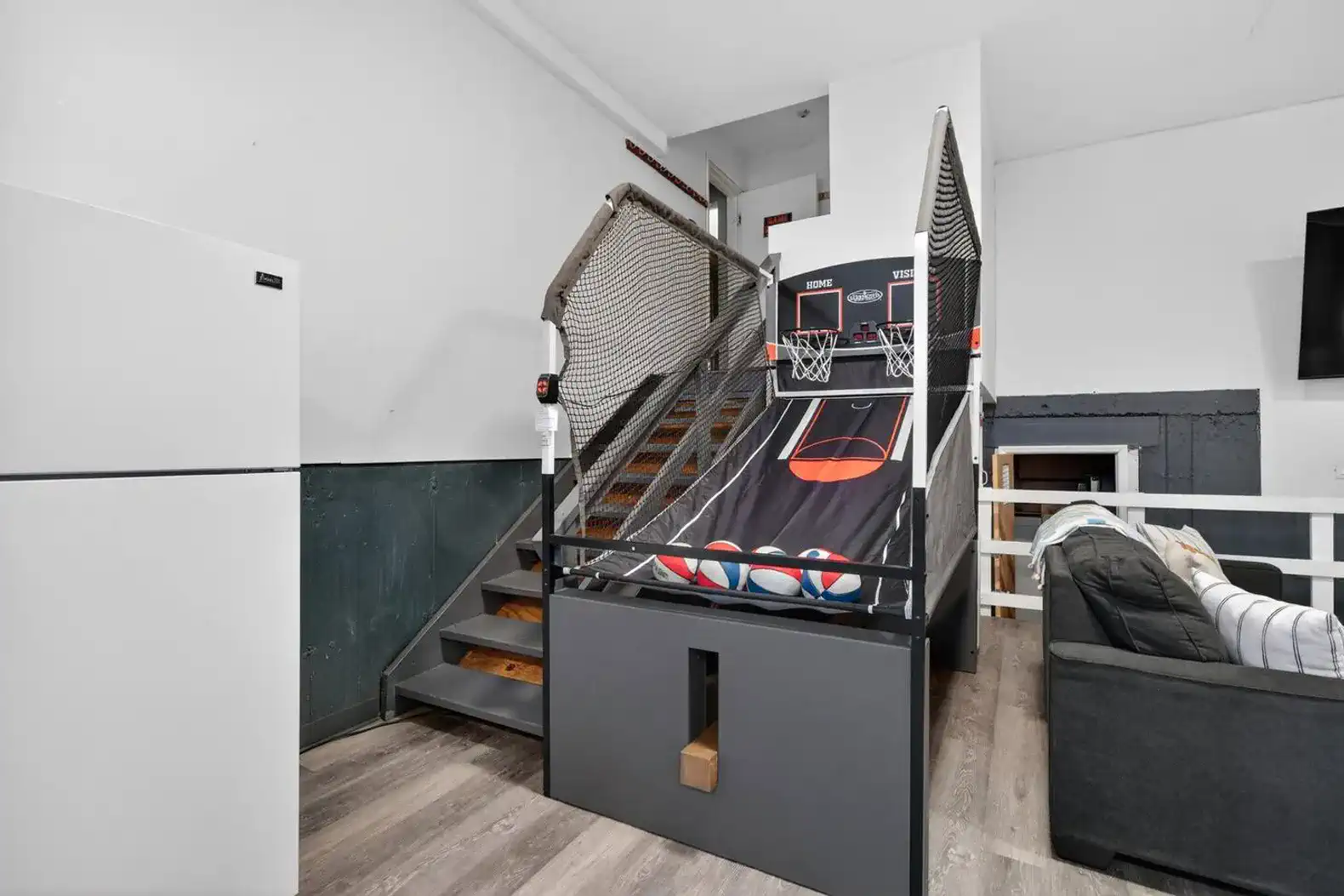 Game lounge with arcade hoops, cozy sofa, TV, and a handy fridge
