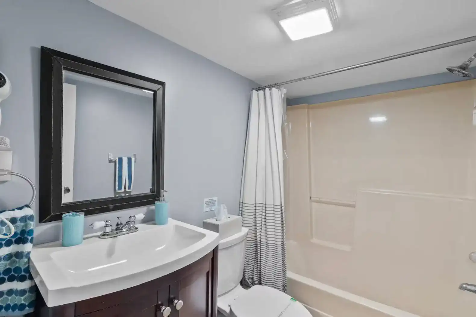 Modern and bright full bathroom with a shower and tub combo, sleek vanity, and fresh blue accents. Designed for comfort and convenience, offering a relaxing space to refresh after a busy day.