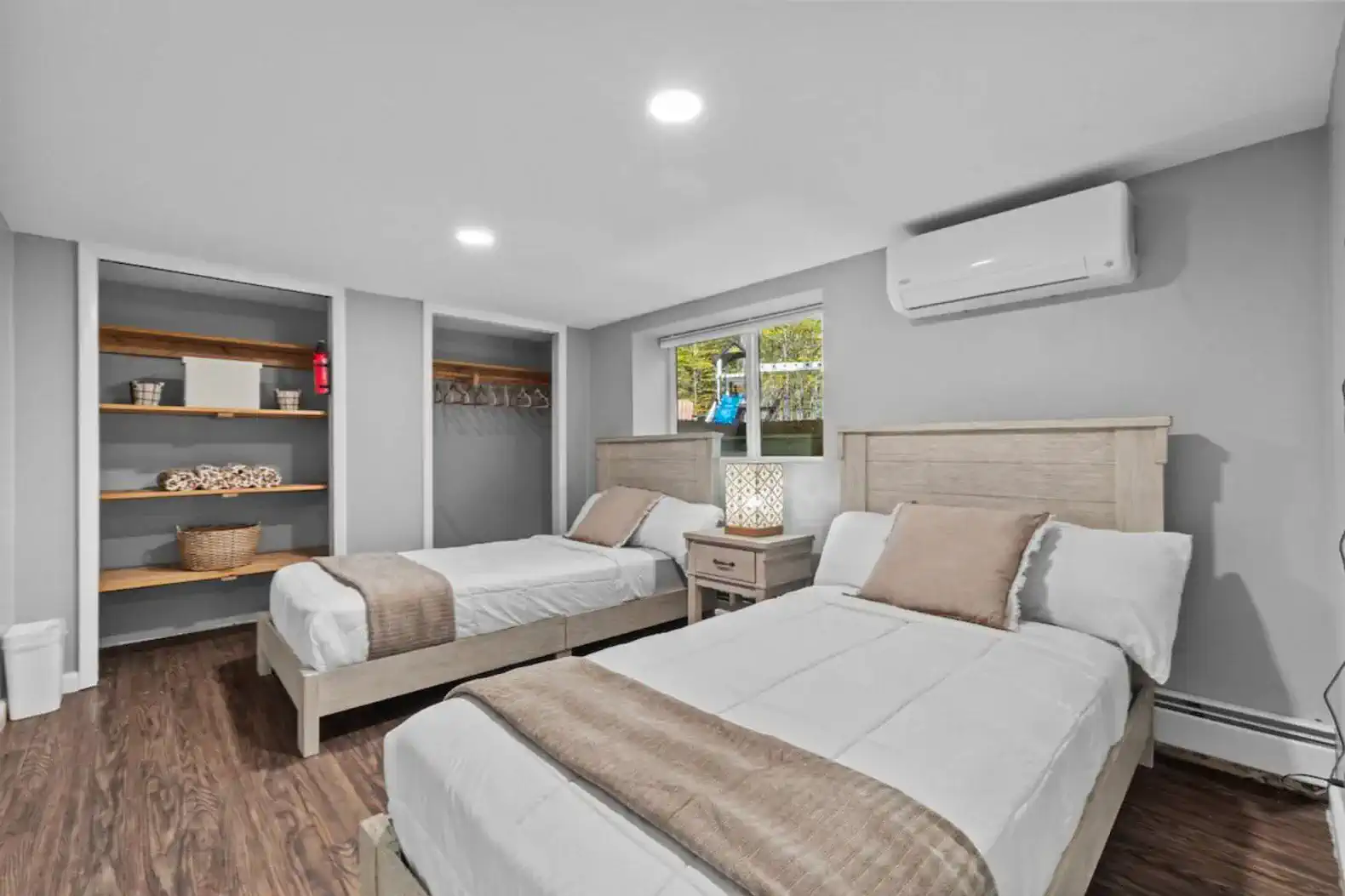 Cozy bedroom with two twin beds, neutral tones, and soft lighting. Features a large window with wooded views and built-in shelving for convenience. Perfect for kids, friends, or additional guests.