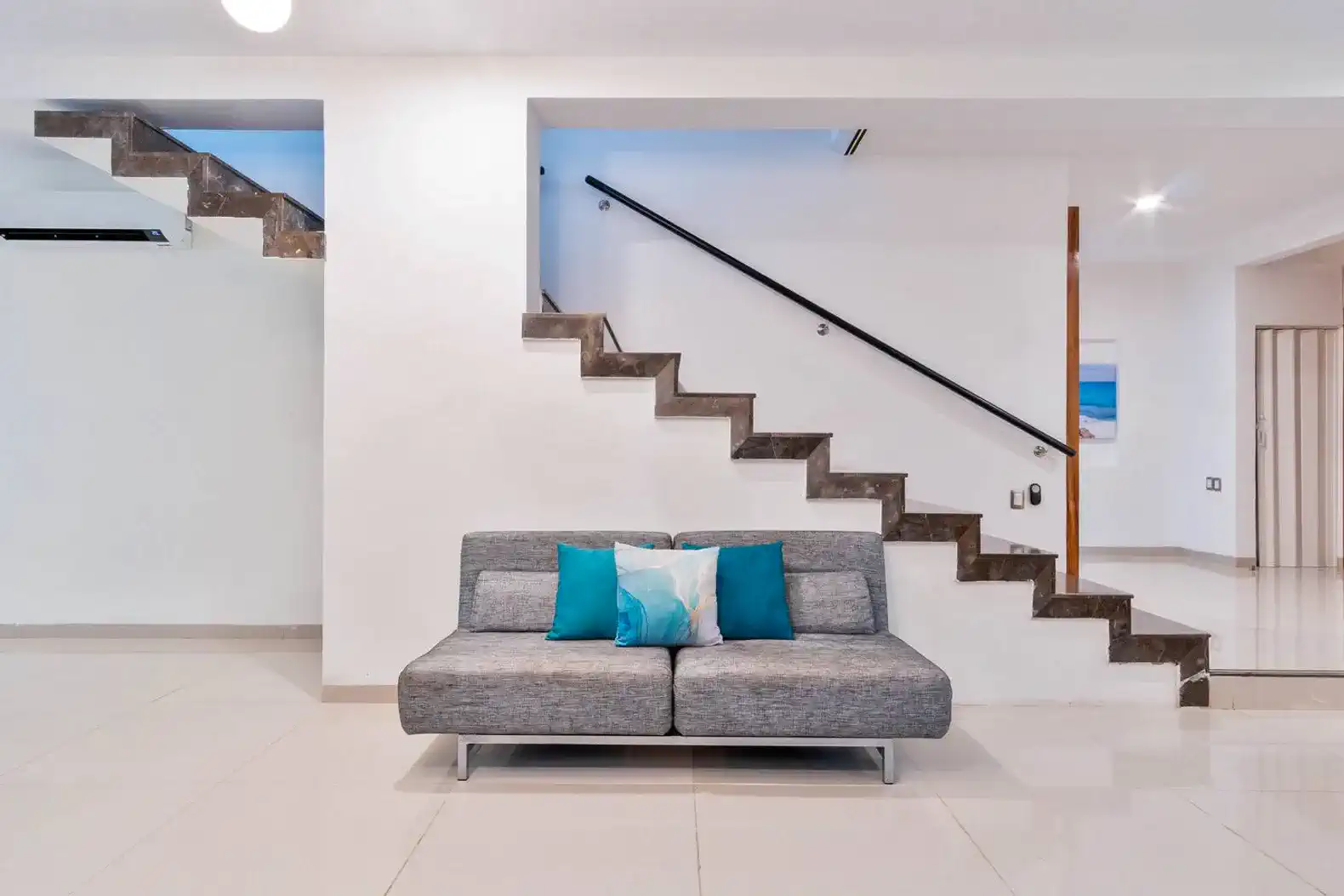 Sala moderna con sofá gris y cojines coloridos junto a escaleras elegantes