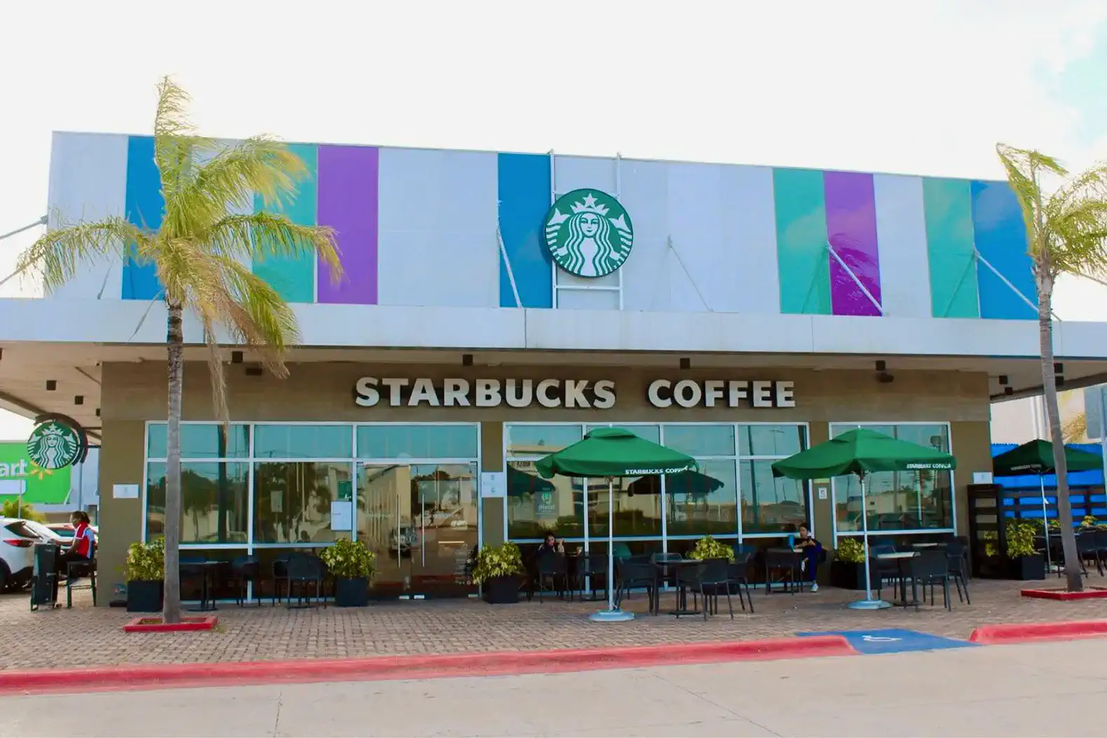 Fachada de Starbucks con sombrillas verdes y palmeras en el exterior