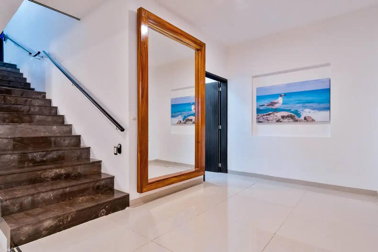 Amplio vestíbulo con escalera y espejo grande, decorado con imágenes de playa