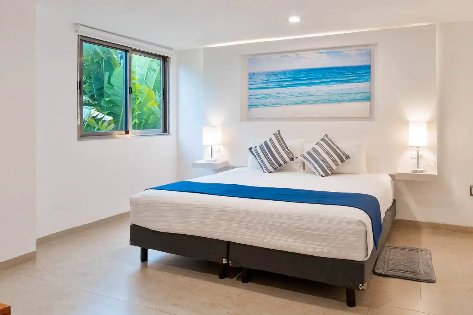 Habitación luminosa con cama grande, ventanas que dan a un jardín tropical
